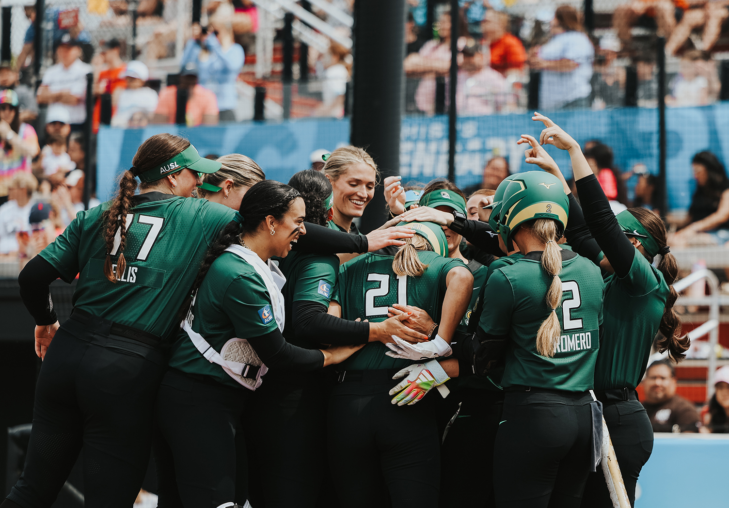 Talons players, including Sharlize Palacios, Montana Fouts, Bri Ellis, and Sydney Romero, in their green jerseys and green visors, celebrate a home run from Sierra Sacco at home plate in front of a sold-out crowd.
